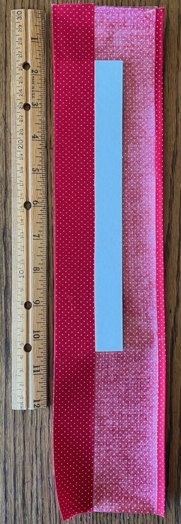 One side of fabric folded over mat board, shown next to a ruler