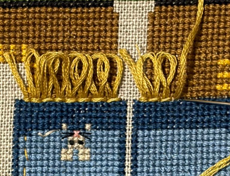 Close-up view of golden-yellow loop stitches in progress at bottom of pant legs