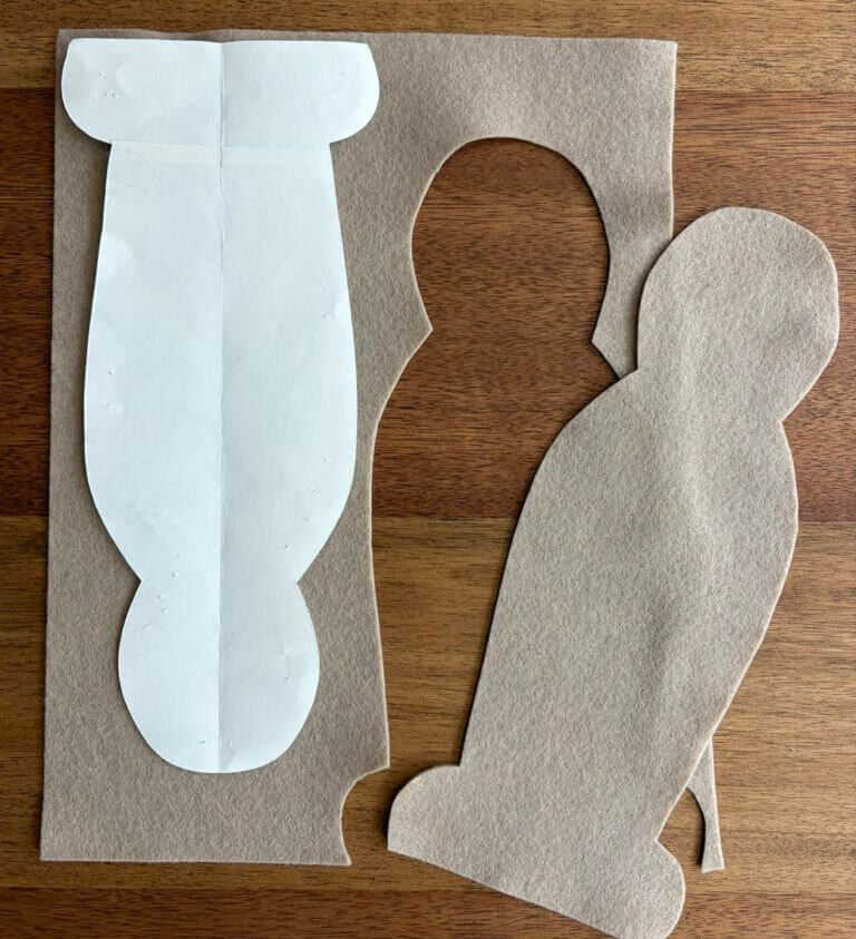 Tan felt sheet with a white paper body template on the left and a matching cut-out felt body shape on the right, on a wooden table