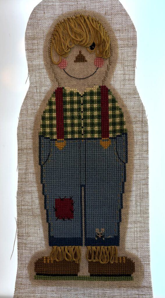 Backlit view of the stitched Harvest Henry figure on linen, with the darker outline of the felt backing visible centered behind him