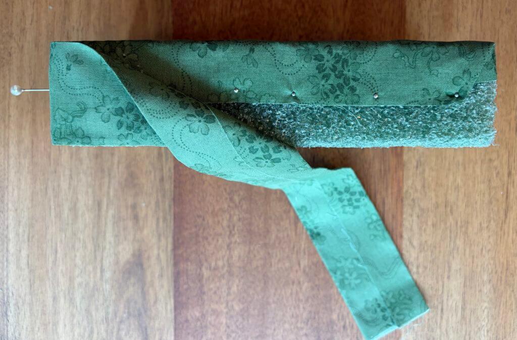 Green foam block with a folded strip of matching floral fabric pinned along the top edge while wrapping the remaining sides