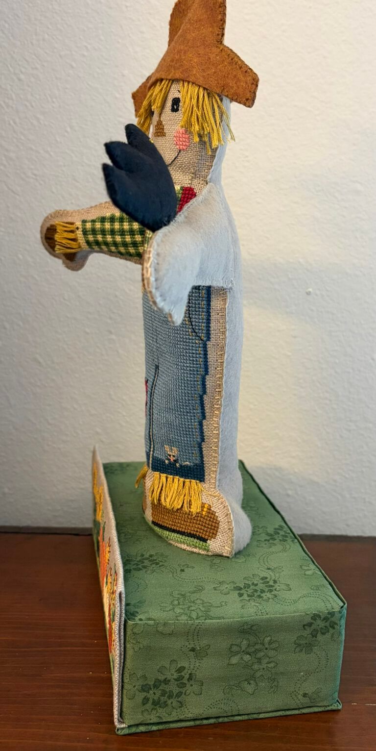 Side profile of finished Harvest Henry on his green fabric-covered stand, showing stuffed depth, brown felt hat, and the pumpkin band on the front of the base